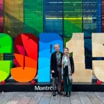 young man and woman stand in front of a colourful sut-out reading COPY15