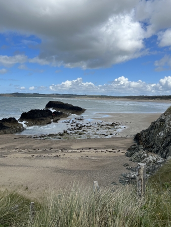 coastal view across sand dune to the sea with some rocks. blue skies with white clouds in the sky