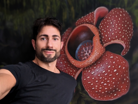 Man with black t-shirt on standing infront of a painting of a flower