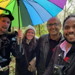 3 mena and a woman with a wolly hat on stand under a multi coloured umbrella